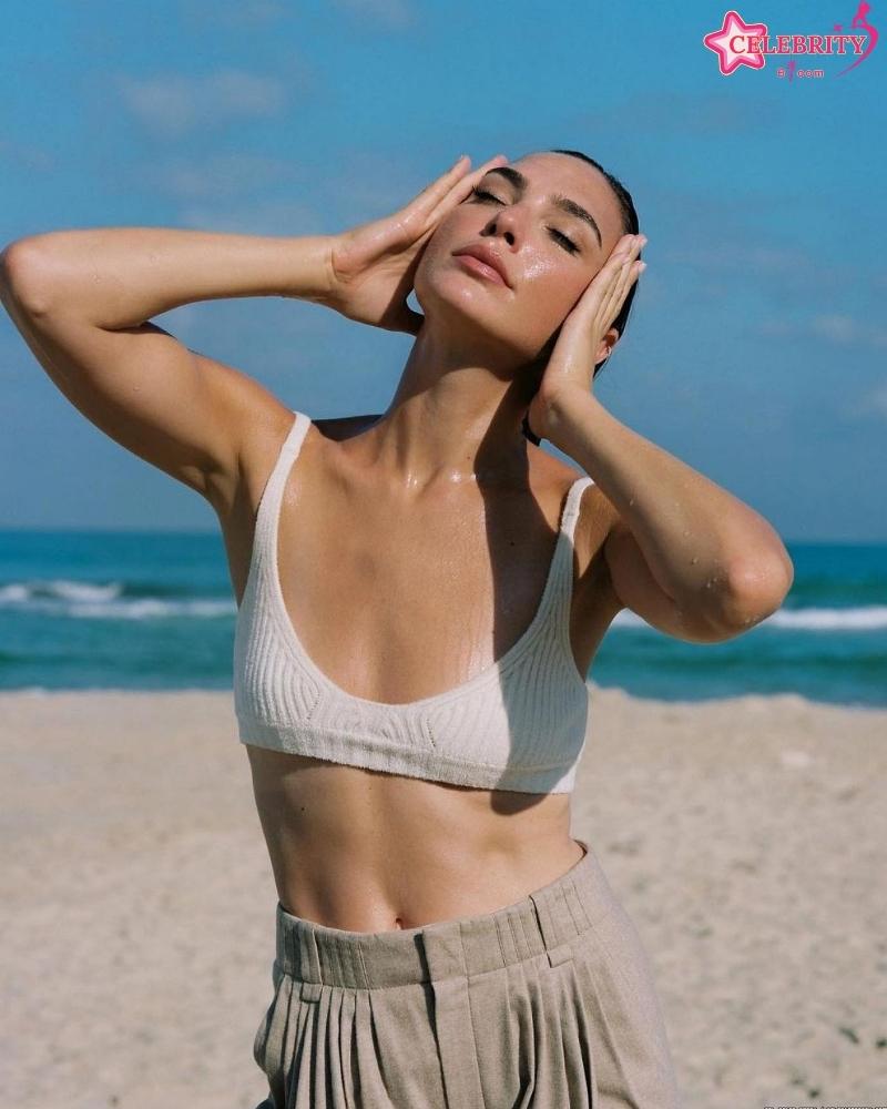 Gal Gadot, wearing a swimsuit, relaxes on a beach.